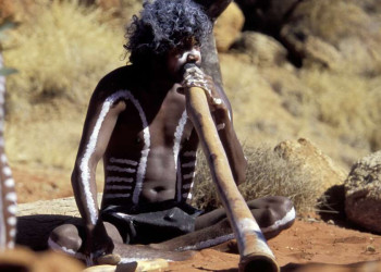Ein Aborigine bläst auf dem Didgeridoo.