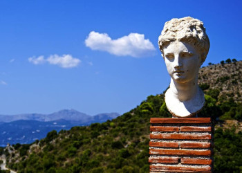 Antike Büste vor bergiger Küstenlandschaft